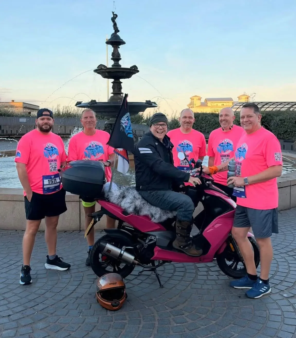 Five runners in pink Scoot 4 Nepal T-shirts standing around Tony Hobden on his pink scooter in front of a fountain in Weston-super-Mare